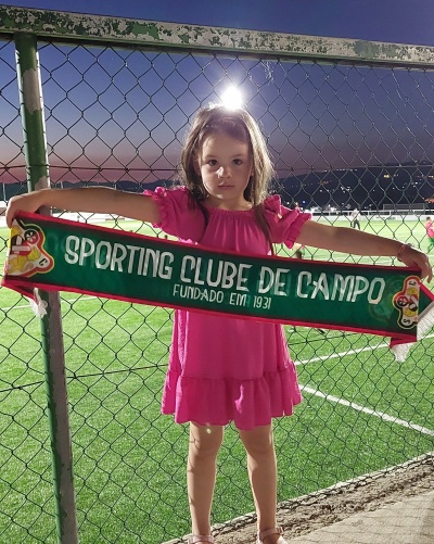 Criança segura faixa do Sporting Clube de Campo num campo desportivo ao entardecer