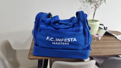Mala desportiva azul F.C. INFESTA MASTERS sobre mesa de madeira com cadeiras e planta