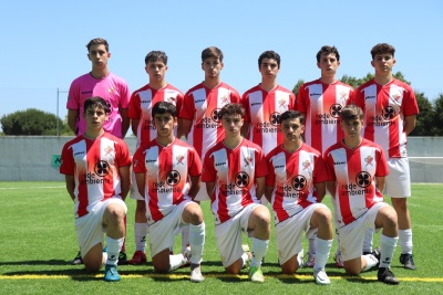 Jogadores jovens de futebol com camisolas vermelhas e brancas e calções brancos num campo relvado