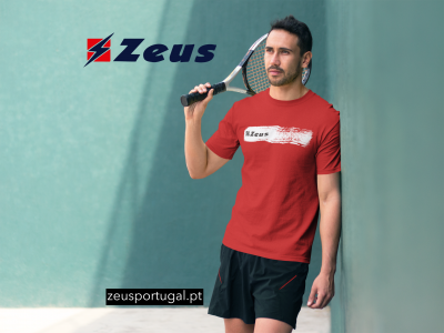 Homem com t-shirt vermelha Zeus e calções pretos segurando raquete de ténis encostado a parede azul.
