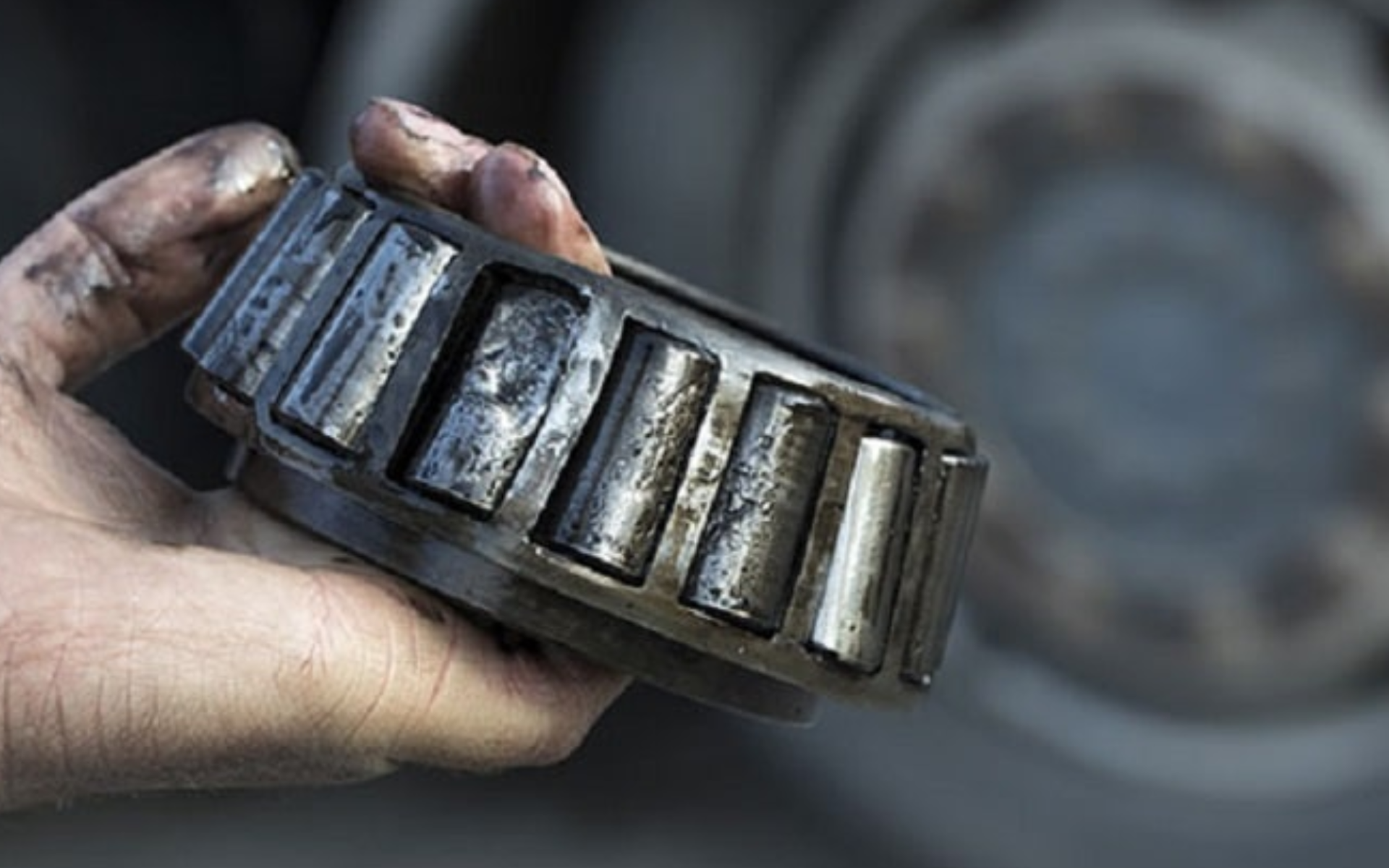 Mão segurando rolamento de metal com rolos cilíndricos
