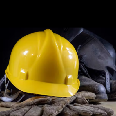 Casco amarelo, luvas castanhas e botas pretas de segurança sobre uma mesa